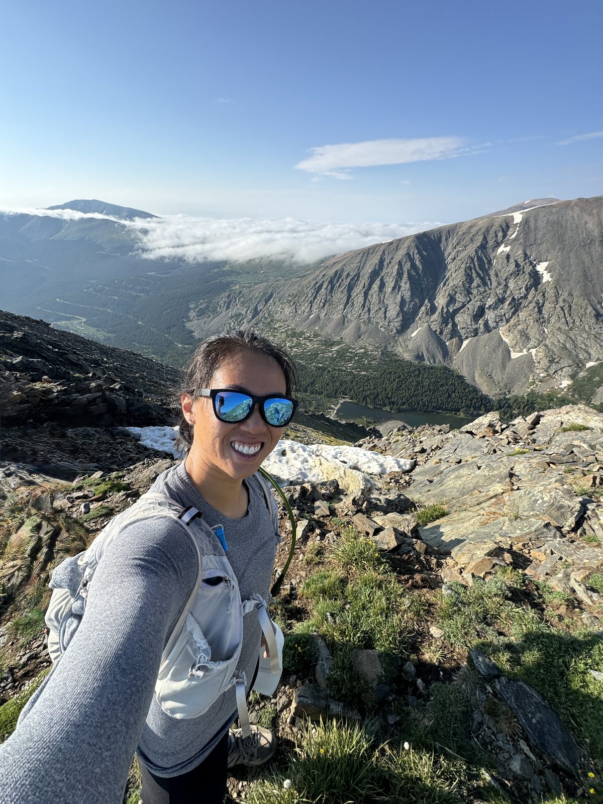 Dr. Erica Tran smiling on a mountain summit above the clouds